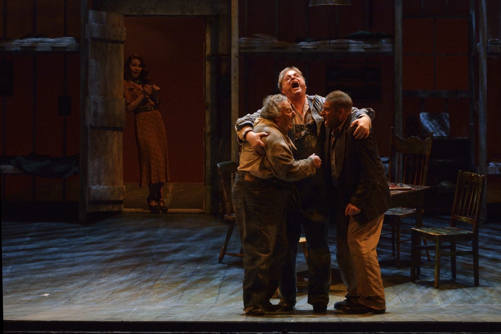 Candy (Peter Strummer, left) and Lennie (Michael Robert Hendrick) and George (Gregory Dahl) celebrate that they can buy a farm as their future downfall, Curley's wife (Nikki Einfeld) watches from the doorway during Manitoba Opera's presentation of "Of Mice and Men". The opera, created by the American composer Carlisle Floyd and based on the John Steinbeck novella runs April 23, 26 and 29 at the Centennial Concert Hall in Winnipeg.